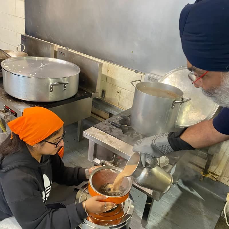 Volunteers work over steaming pots on gas burners in the gurdwara kitchen.