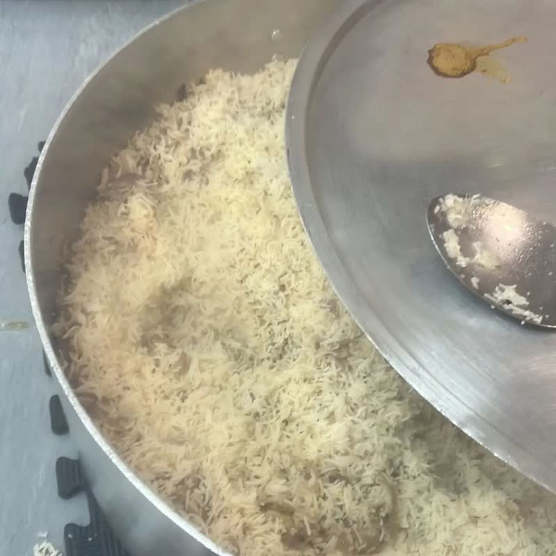 Close-up of a large steel pot full of freshly cooked white rice, the lid tipped to one side.
