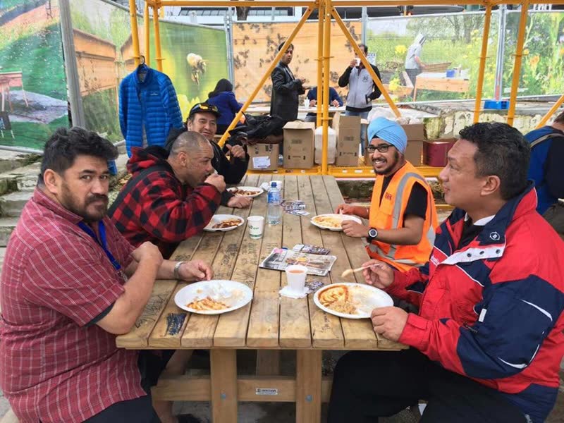 People of different ages sit together along a wooden table, eating and talking.